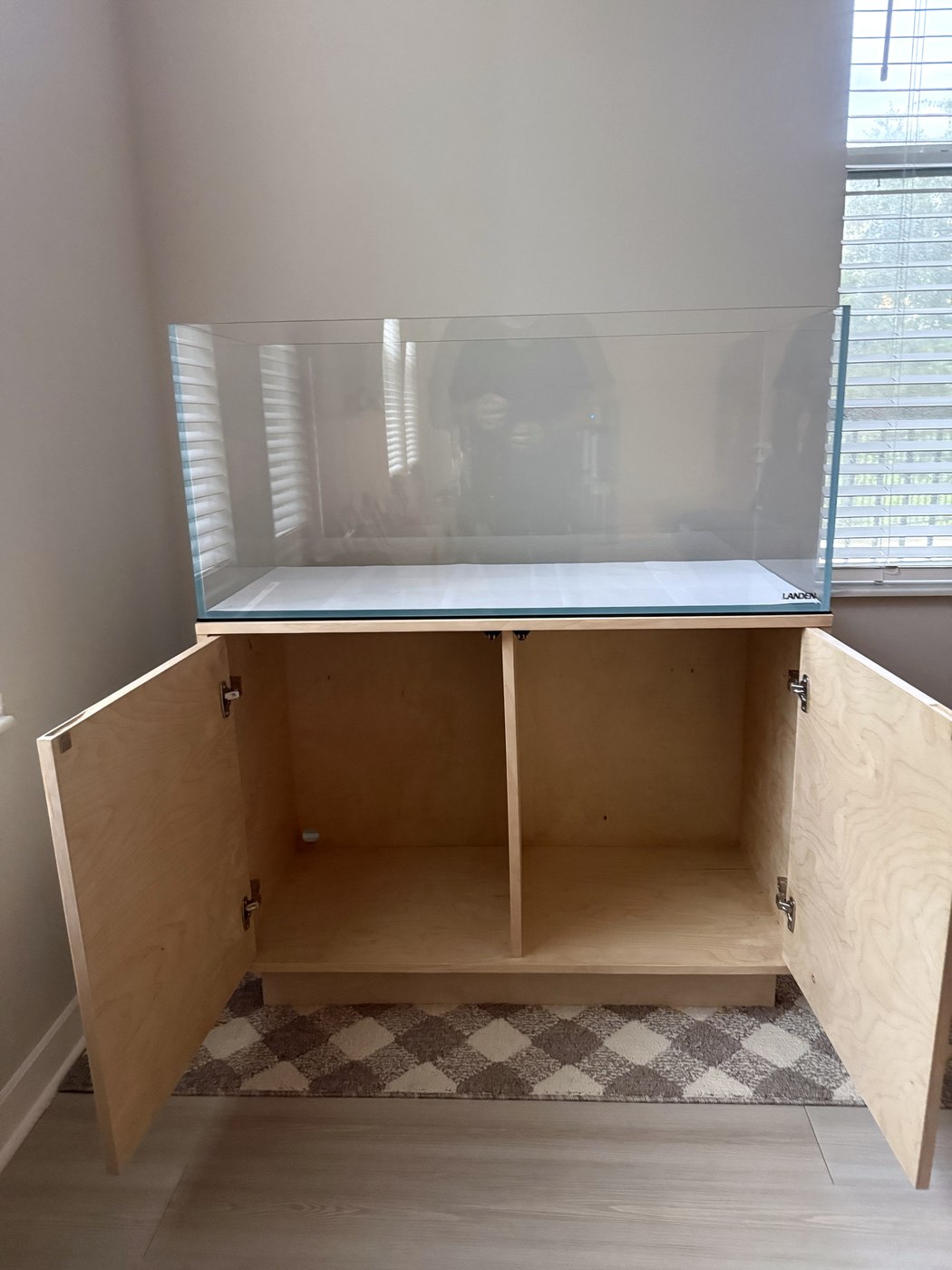 Birch plywood aquarium stand with both doors open showing a divided interior, supporting a rimless glass aquarium.