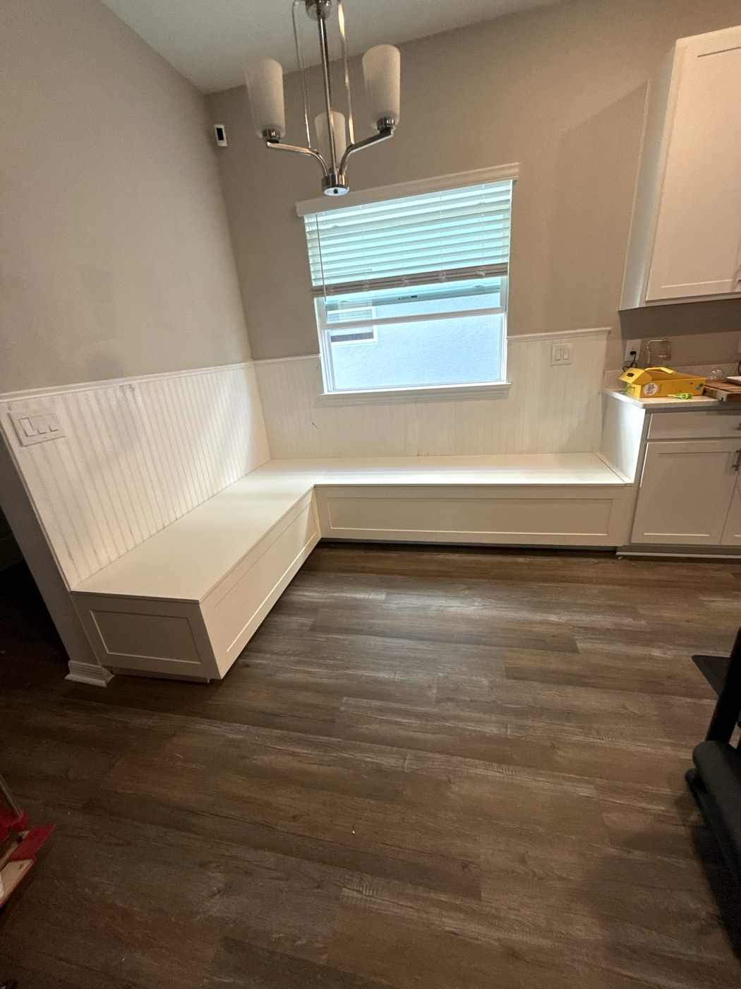 White painted L-shaped built-in banquette bench in a breakfast nook, with beadboard backing, shaker panel detail and hidden storage under the seats.