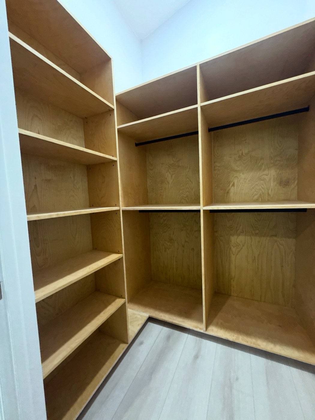 Custom walk-in closet system built from birch plywood, with adjustable shelving, double-hang sections and blackened steel hanging rods.